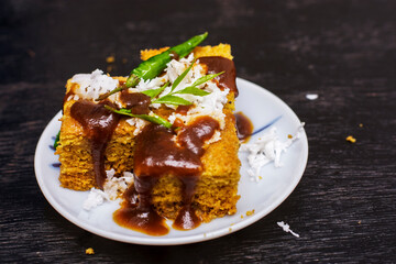 Gujarati khaman Dhokla made with chana dal served with coconut and chutni on a white plate and black background.