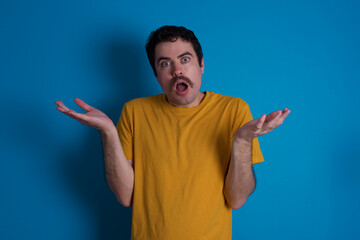 Frustrated young handsome Caucasian man with moustache wearing yellow t-shirt  feels puzzled and...