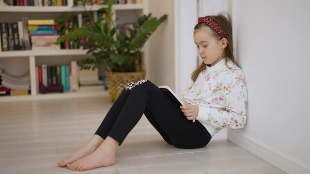 Preschooler girl reading book in home library