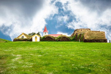 Green grass, church and old houses in traditional Icelandic Village with blue sky and clouds around,
