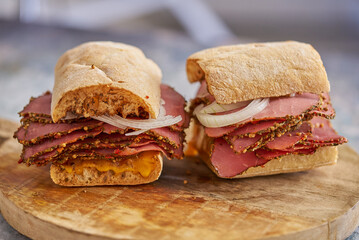 Thin cut pastrami sandwhich with delicious meet on baguette bread with chedder cheese, onion