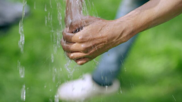 Close-up African American male hands washing with water outdoors on sunny day. Unrecognizable young man cleaning palms after working in garden on spring. Gardening and landscaping