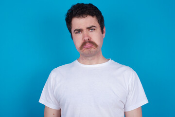 young handsome Caucasian man with moustache wearing white t-shirt against blue background depressed and worry for distress, crying angry and afraid. Sad expression.