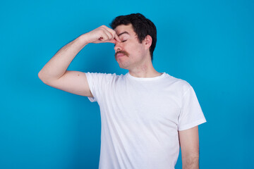 Obraz premium Sad young handsome Caucasian man with moustache wearing white t-shirt against white background suffering from headache holding hand on her face