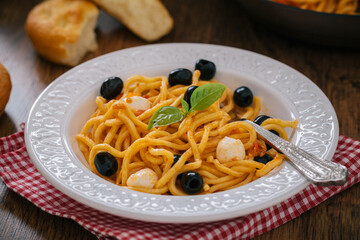 Spaghetti with tomato sauce, black olives, mozzarella and basil on a plate
