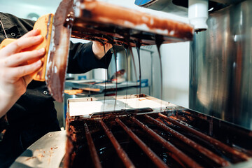 detail on hands of female master chocolatier pouring liquid chocolate from the stamp into tempering...