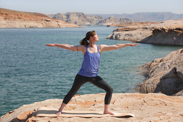 woman practicing yoga outdoors by a lake in warrior pose