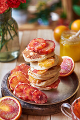Pancakes with red oranges on a background of green plants and red flowers. Side view.