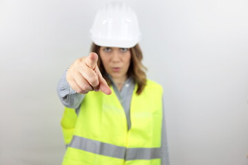 Woman engineer with hardhat pointing displeased and frustrated to the camera, angry and furious at you. Face bokeh.