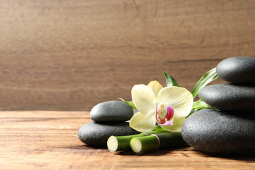 Fototapeta na wymiar Spa stones, bamboo stems and beautiful orchid flower on wooden table, space for text