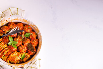 Homemade meatballs with tomato sauce in a white dish baked in the oven with herbs on marble white background