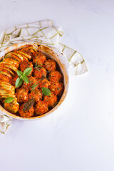 Homemade meatballs with tomato sauce in a white dish baked in the oven with herbs on marble white background