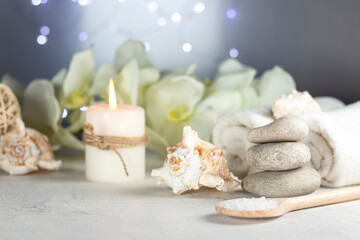 Fototapeta na wymiar massage stones, seashell, burning candles, rolled towels, sea salt, flowers, abstract lights. Spa resort therapy composition