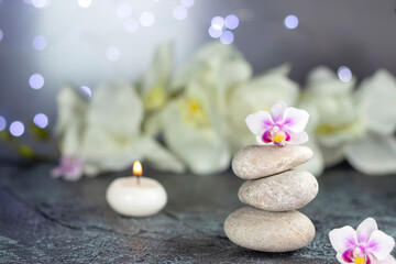 Fototapeta na wymiar Spa resort therapy composition. Stones, burning candles, orchid flowers, towel, abstract lights