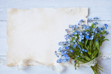 Bouquet of forget-me-not flowers and paper for the text congratulations on a white wooden background.