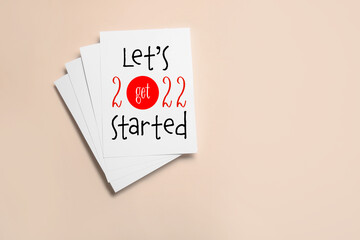 Paper sheets with text LET'S GET 2022 STARTED on color background