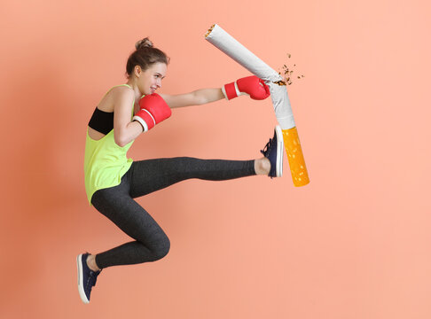 Jumping sporty woman in boxing gloves kicking cigarette on color background