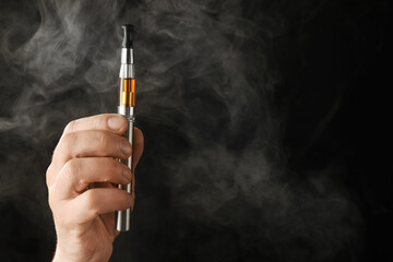 Male hand with electronic cigarette on dark background with fume