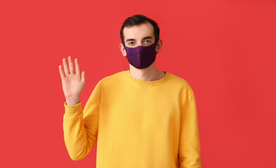 Obraz premium Young man wearing medical mask and waving hand on color background