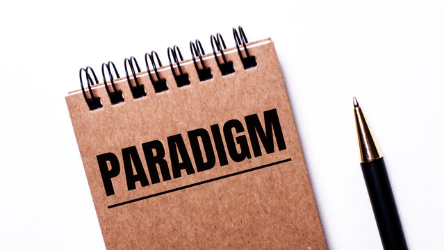 On a light background, a black pen and a brown notebook on black springs with the inscription PARADIGM