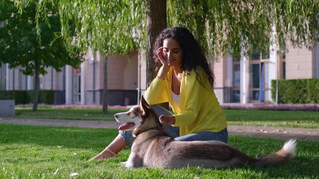 rest in park with dog, young woman and her pet are sitting on green grass