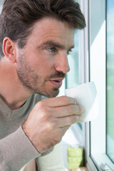 man stood by window holding coffee sup