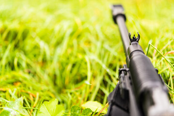 Aiming a rifle in the grass covered with morning dew. Close up view from ground level