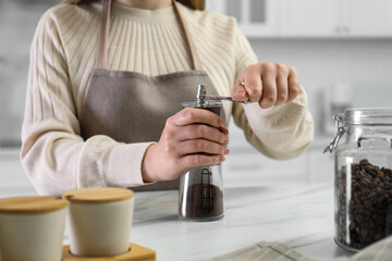 Woman using coffee grinder at table indoors, closeup