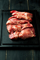 Raw meat on a black cutting board on a dark background - 433821869