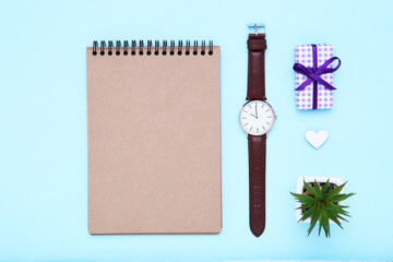 Father's day concept. Notepad with wrist watch, gift box and green plant on blue background