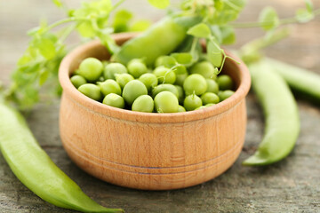 Peas on bowl with green stem on wooden table