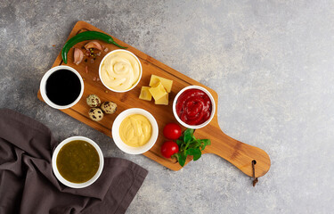 Assortment of sauces, ketchup, mayonnaise, cheese, soy, green, on a cutting board, with ingredients, on a gray table, top view, no people,