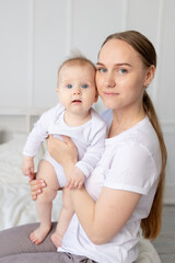 portrait of a mother with a baby in her arms gently embracing him on a white bed at home, mother's love
