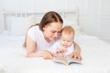Fototapeta na wymiar mom reads a book to baby before going to bed on a white bed with cotton bedding at home, happy family