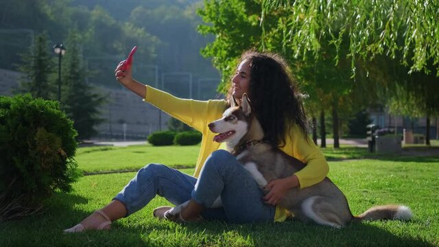 young woman is taking selfie with her dog in park by smartphone