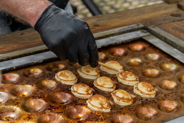close up of a male baker preparing fresh the sweet Dutch batter treat called Poffertjes on a special griddle
