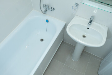 Small bathroom with white bathtub. New snow-white plumbing in bathroom. Plumbing sale concept. Plumbing installation and maintenance. Bathroom and sink are shiny due to cleaning products