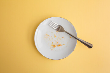 Dessert crumbs in white round plate with fork on yellow background, top view - Powered by Adobe