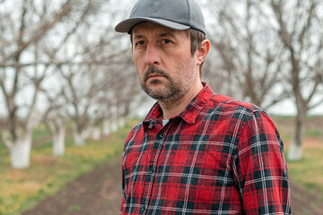 Naklejka na ściany i meble Portrait of handsome confident farmer with baseball cap and flannel shirt in walnut fruit orchard