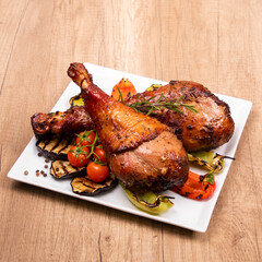 Grilled chicken with vegetable garnish served in a white plate on wooden table. Copy space, square format.