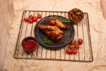Grilled turkey chicken leg on wooden round cutting board with some greens and spices. Served on craft paper, fried potato slices with garlic, tomato juice and cherry tomatoes. 