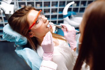 Young woman opening her mouth wide during treating her teeth by the dentist. Hands of a doctor...