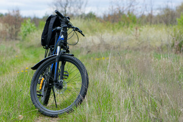 Obraz premium bike stands on in the field. A mountain bike stands on a field path with green grass. outdoor cycling activities. space for text. concept of cycling, repair or breakage, sports, outdoor activities