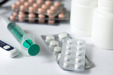 syringe, thermometer, pills in plates, in white jars on a light background, medical concept