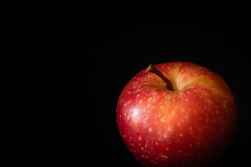 Fresh ripe red apple with water drops on glossy peel on black background