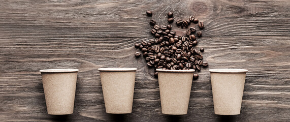 Coffee paper cups and one cup with coffee beans on a wooden background. Background template and creative concept for cafe, coffee shop. Advertising banner with place for text 
