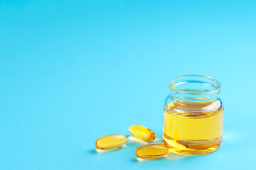 Jar and capsules with yellow cosmetic oil on a blue background.