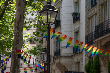 Decoration of triangle shape banners in colors of Lgbtq flags hanging between vintage lantern streetlights and ornate stone house with balconies. Gay pride parade in Paris France