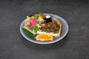 Apiece of vegetarian and vegan pizza, light breakfast with salad and orange gray plate, and dark background.