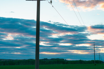 Naklejka na ściany i meble Electric pillars with wires and pink sky with clouds at sunset.